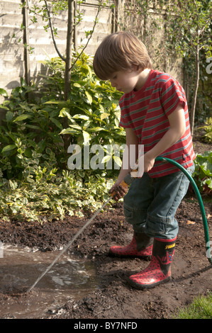 Garçon jouant avec le soutien de faire une flaque d'eau et de boue dans le jardin arrière. quatre-année-vieux Banque D'Images