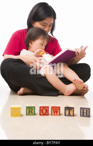 Mère et sa petite fille lecture livre avec bloc avec word "Croissance" disposés en face d'eux Banque D'Images