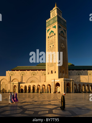 L'homme et de la femme marocaine la marche sur la plaza de la Mosquée Hassan II Casablanca au coucher du soleil avec minaret de l'architecture mauresque à Casablanca Maroc Banque D'Images