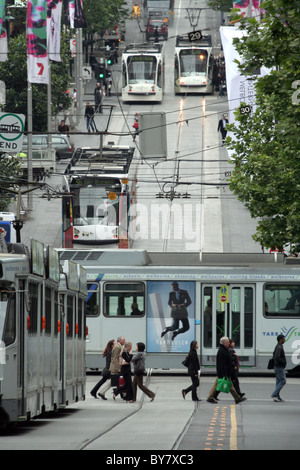 Voir le long d'une rue animée avec de nombreux trams (light rail) et les piétons qui traversent la route, Melbourne, Victoria, Australie. Banque D'Images