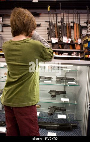 Garçon de huit ans à la recherche de fusils et carabines dans un magasin d'armes, United States. Banque D'Images