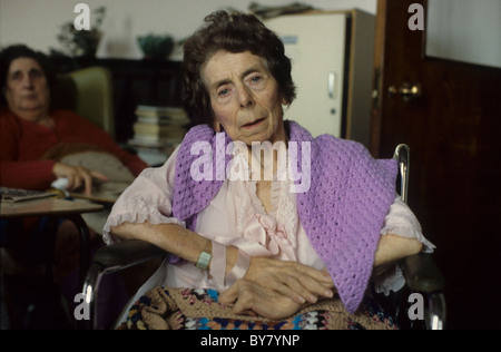 Une femme âgée qui cherche un appareil photo portant un violet mauve crocheted châle assis près de sa table de chevet dans un Service hospitalier au pays de Galles, Royaume-Uni KATHY DEWITT Banque D'Images