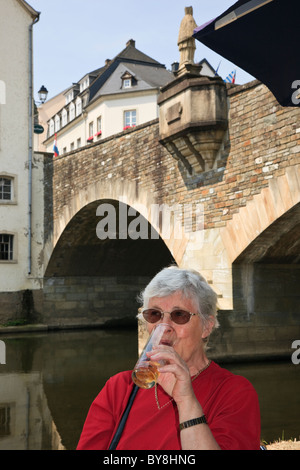 Une femme de tourisme senior buvant un verre de bière dans un café en plein air en pont au-dessus de la rivière Notre. Vianden, Grand-Duché De Luxembourg Banque D'Images