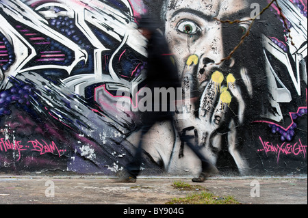 Homme marchant passé mur graffiti Banque D'Images