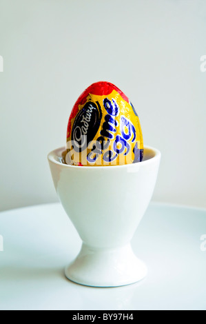 Un Cadbury Creme Egg in a white egg cup sur une plaque blanche. Banque D'Images