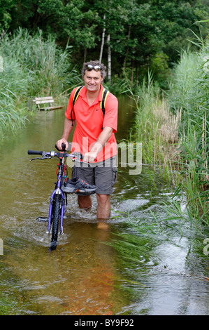 Cycliste en poussant son vélo à travers un chemin inondé sur les rives du lac Simssee, Chiemgau, Upper Bavaria, Germany, Europe Banque D'Images