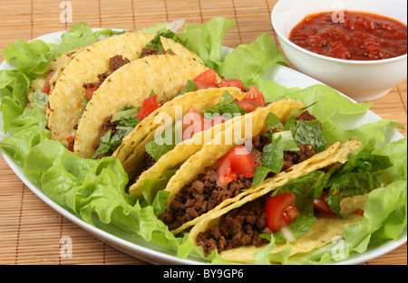 Rangée de tacos remplis de boeuf sur un lit de laitue servis avec une trempette salsa de tomate Banque D'Images