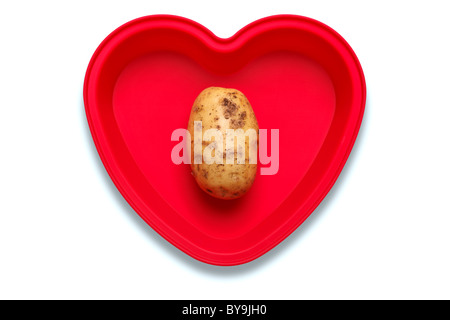 Photo conceptuelle d'une pomme de terre dans un plat en forme de coeur pour représenter un amour de la légume, isolé sur fond blanc Banque D'Images