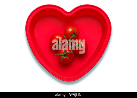 Photo conceptuelle des tomates dans un plat en forme de coeur pour représenter un amour de la légume, isolé sur fond blanc Banque D'Images