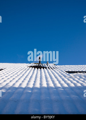 Une combinaison de fumée Chaudière domestique sur un toit à vapeur émettant sur un toit couvert de neige contre un ciel bleu clair. Banque D'Images