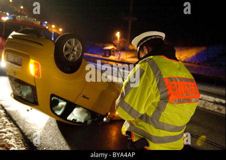 Agent de police de prendre les détails en face d'une voiture renversée après un accident sur une route glacée, road B 14, Stuttgart Banque D'Images