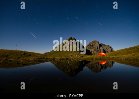 Photo de nuit, illuminé tente reflétée dans le Berglimatt Lake par la lumière de la pleine lune, canton de Glaris, Suisse, Europe Banque D'Images