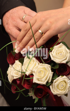 Concept de mariage montrant deux mains sur le haut d'une rose rouge et blanc arrangement floral. Banque D'Images