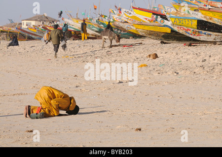 Pêcheur de prier vers La Mecque en face de l'bateaux colorés dans le port de pêche de Nouakchott La Mecque, Afrique de l'Ouest Banque D'Images