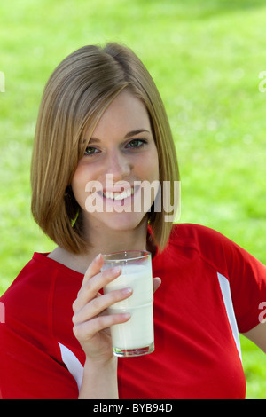 Jeune femme portant des vêtements de sport avec un verre de lait à la main, smiling Banque D'Images