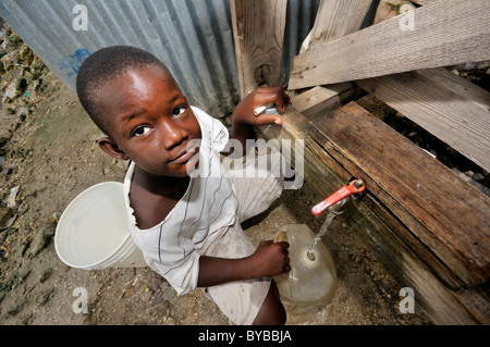 Installation de traitement de l'eau potable dans un bidonville, le remplissage de l'eau propre garçon dans un jerrican, , Haïti, Caraïbes, Amérique Centrale Banque D'Images