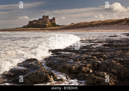 Château de Bamburgh vue de la plage vers le nord, à travers les rochers à marée montante. Banque D'Images