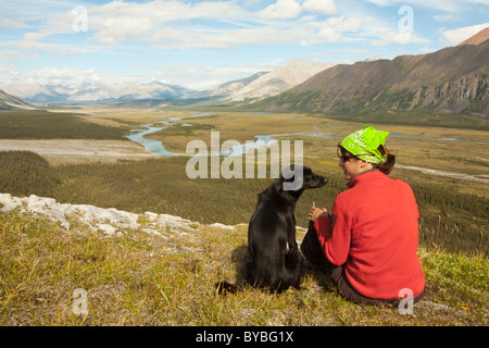 Jeune femme assise, se reposer, profiter de la vue, panorama, Alaskan Husky, chien de traîneau à côté d'elle, Wind River valley et Mackenzie Banque D'Images