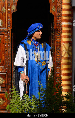 Profil de l'habillement bleu traditionnel berbère de Taureg homme debout en bois sculpté orné porte dans médina de Marrakech Maroc Banque D'Images