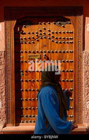 La femme en bleu marcher par la porte d'ocre rouge et le mur d'une maison dans le souk de Marrakech Maroc Banque D'Images