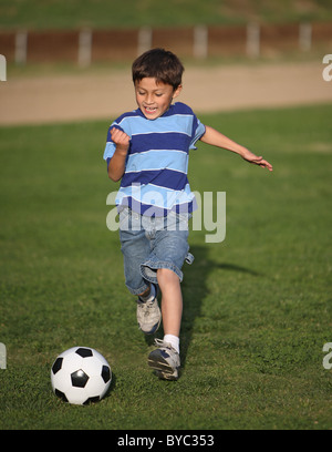 Heureux garçon Latino authentique jouant avec un ballon de soccer dans la zone portant des tee shirt rayé bleu. Banque D'Images