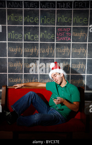 Man with Santa hat/elf et martini verre d'alcool dans la main endormie en face de Noël Décembre Calendrier coquin et agréable. Banque D'Images