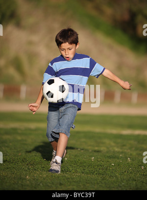 Heureux garçon Latino authentique jouant avec un ballon de soccer dans la zone portant des tee shirt rayé bleu. Banque D'Images