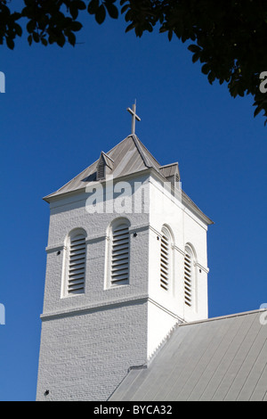 Vieux clocher de l'église du pays contre un ciel bleu et photographié de sous les arbres. Banque D'Images