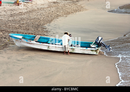 Pêcheur barefoot travaille sur son bateau à la fin de l'après-midi que les ondelettes lap le sable doré de la plage de Puerto Angel beach dans l'état d'Oaxaca au Mexique Banque D'Images