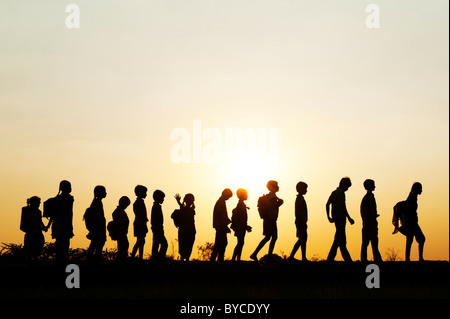 Filles et garçons indiens Silhouette marcher à la maison de l'école à travers un champ de riz au coucher du soleil. L'Andhra Pradesh, Inde Banque D'Images