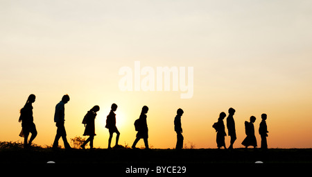 Filles et garçons indiens Silhouette marcher à la maison de l'école à travers un champ de riz au coucher du soleil. L'Andhra Pradesh, Inde Banque D'Images