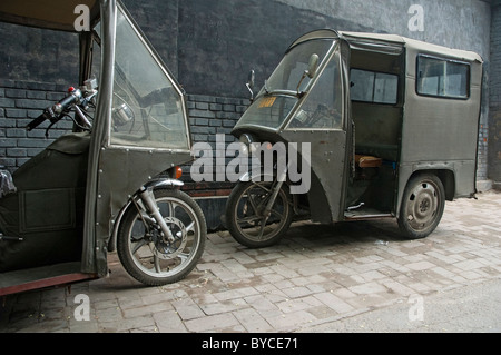 Les tricycles à moteur en stationnement deux contre un mur de brique grise, quartier de Hutong, Beijing, Chine. Banque D'Images