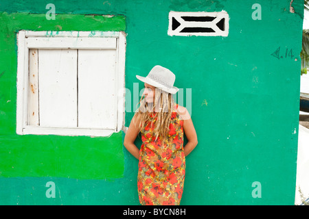 Femme avec des dreadlocks blonde en robe rouge et blanc hat appuyé contre un mur vert au Panama Banque D'Images