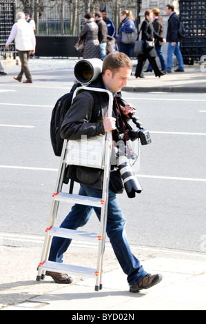 Photographe mâle caméras et objectifs photographiques avec équipement de marche de l'échelle à l'extérieur de la chaussée chambres du Parlement London England UK Banque D'Images