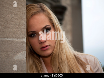 Jeune femme avec de longs cheveux blonds soigneusement appuyé contre un mur, portrait Banque D'Images