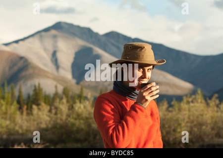 Jeune femme à boire, prendre une tasse de thé, Wind River, dans le nord des monts Mackenzie derrière, Territoire du Yukon, Canada Banque D'Images