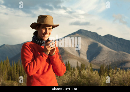 Jeune femme à boire, prendre une tasse de thé, Wind River, dans le nord des monts Mackenzie derrière, Territoire du Yukon, Canada Banque D'Images