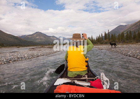 Jeune femme à bord de canots, canoë, Wind River, dans le nord des monts Mackenzie, chien sur la rive, Territoire du Yukon, Canada Banque D'Images