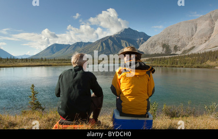 Couple, homme et femme, assis sur la rive, appréciant la vue, panorama, Wind River Valley, dans le nord des monts Mackenzie Banque D'Images