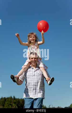 Père en portant sa fille sur ses épaules alors qu'elle est maintenant un ballon Banque D'Images
