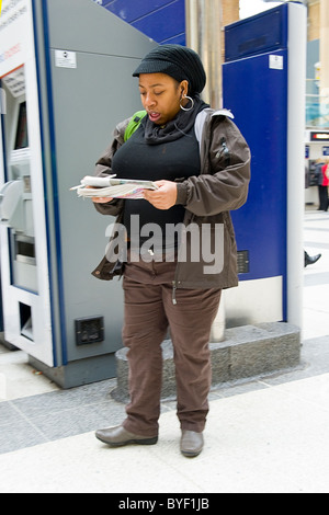La gare de Liverpool Street , LONDRES , noir ou de couleur en fille Afro Antillais ont atteint un sommet en tricot hat lecture par ticket machine Banque D'Images