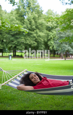 Jeune homme aux cheveux afro lying in hammock in park Banque D'Images