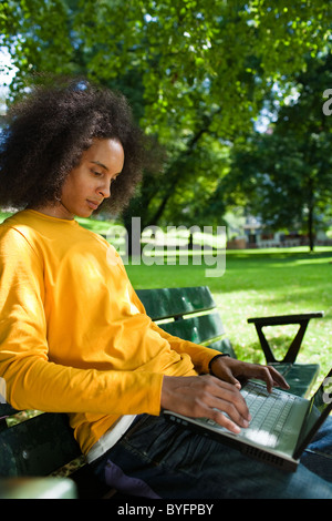 Jeune homme aux cheveux afro assis sur un banc et using laptop Banque D'Images