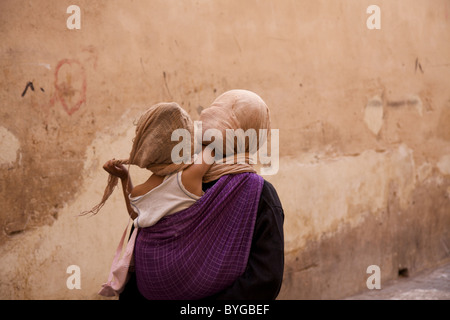 Une femme avec un enfant sur le dos de promenades à travers les souks de la medersa Ben Youssef, Marrakech Medina, Maroc, afrique du nord Banque D'Images