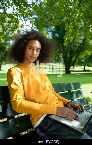 Jeune homme aux cheveux afro assis sur un banc avec coffre Banque D'Images