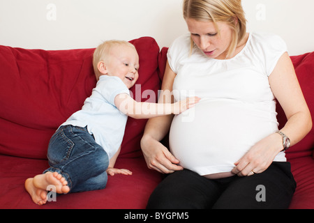 Garçon de toucher les mères enceintes estomac sur canapé Banque D'Images