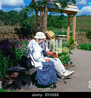 Un couple de personnes âgées portant des chapeaux de paille assis sur un banc, lisant un livre au Jardin Botanique National du Pays de Galles UK KATHY DEWITT Banque D'Images