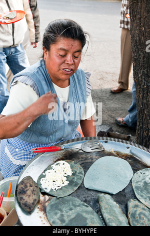 Cuisinier mexicain génial en tablier Vichy bleu impeccable sur son travail de brazier tacos de maïs bleu sur trottoir quartier rom de Banque D'Images