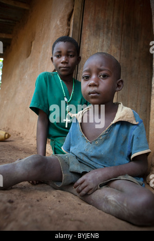 Les enfants sont assis à l'extérieur de la porte de leur maison de terre dans les régions rurales de Masaka, en Ouganda, en Afrique de l'Est. Banque D'Images