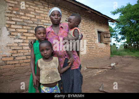 Une jeune mère célibataire et ses enfants devant leur maison de brique, dans les régions rurales de Masaka, en Ouganda, en Afrique de l'Est. Banque D'Images